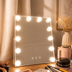 Puede incluir: Un espejo de tocador rectangular con doce bombillas LED redondas integradas a lo largo del marco. El espejo cuenta con tres iconos de control táctil etiquetados como M, un símbolo de encendido y P en la parte inferior central del cristal.