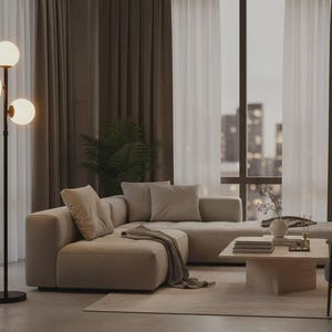 May include: A tall floor lamp with a thin black metal pole and three spherical white glass shades arranged at different heights. The lamp emits a warm glow, standing on a circular black base, providing illumination in a living room setting.