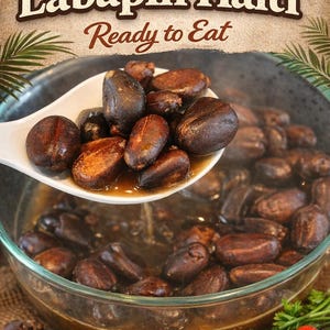 May include: A close-up of a clear glass bowl filled with Labapin Haiti, a Haitian dish. A white spoon holds several dark brown, oval-shaped beans. The text "Pre Boil Labapin Haiti Ready to Eat" is at the top of the image.
