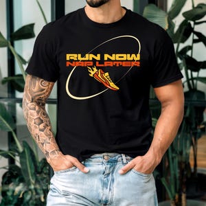 Könnte beinhalten: Schwarzes T-Shirt mit einer gelben und orangenen Grafik eines Laufschuhs und dem Text "Run Now Nap Later".