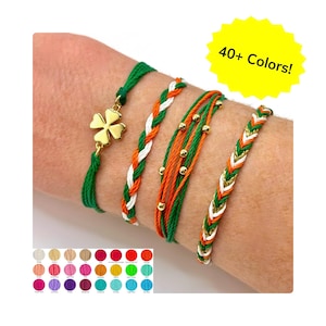 May include: A collection of colorful friendship bracelets in green, orange, white, and gold. One bracelet features a gold clover charm. The image includes a color chart with over 40 color options. Text on the image reads "40+ Colors!"