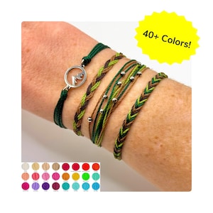 May include: A collection of colorful bracelets in shades of green, brown, and silver. One bracelet features a mountain charm. The image includes a color chart and text that reads "40+ Colors!"