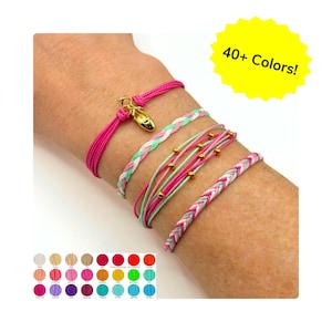 May include: A collection of colorful bracelets on a wrist. One bracelet is hot pink with a gold ballet shoe charm. Other bracelets are braided or strung with gold beads. The image includes a color chart and text that reads "40+ Colors!"