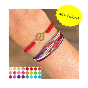 May include: Two bracelets are shown. One is red with a gold-colored charm. The other bracelet has red, white, and blue cords with gold-colored beads. The image includes a color palette with 40+ colors.