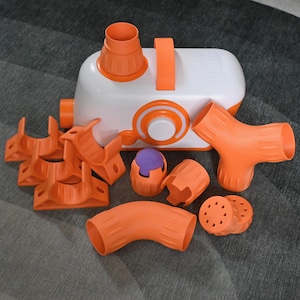 May include: A white and orange toy set with various components, including a central unit, connectors, and tubes. The set features a handle and circular design elements. The pieces are orange and white, with a purple ball.