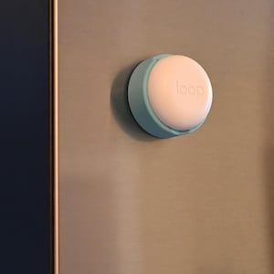 May include: A white and light blue circular object with the word "loop" printed on it. The object is mounted on a gray surface. The object has a light blue ring around a white circular center.