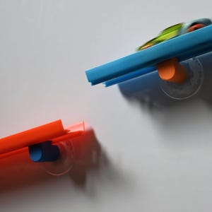 May include: Two colorful, plastic, wall-mounted organizers. One is bright orange, the other is blue. Each has a suction cup for attachment. The organizers are designed to hold small items and are ideal for a bathroom or office.