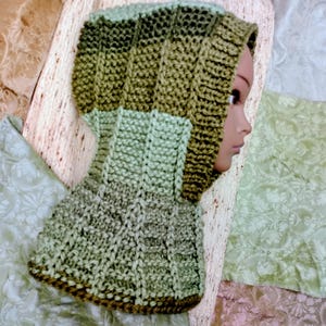 May include: A knitted hood in shades of green and brown. The hood is made of a textured yarn and features a ribbed design on the top and a patterned stitch on the lower portion. The hood is displayed on a mannequin head.