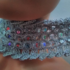 May include: A silver crochet choker necklace with the word "POWERFULNESS" spelled out in colorful letters.