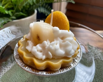 May include: A yellow lemon scented candle shaped like a key lime pie with a white whipped cream topping and a pear slice on top.