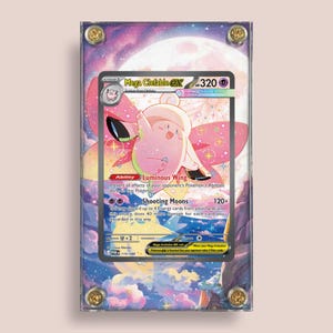 May include: A framed Mega Clefable EX Pokémon trading card. The card features a pink and white Clefable with a large moon and starry background. The card is encased in a clear acrylic case with gold-colored screws at each corner.