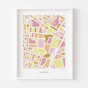 Könnte beinhalten: Ein gerahmter Druck mit einer stilisierten Karte von Austin, Texas. Die Karte verwendet ein geometrisches Design mit Farbblöcken in Rosa, Gelb und Braun. Das Wort "AUSTIN" ist unten in einfacher Schrift gedruckt.