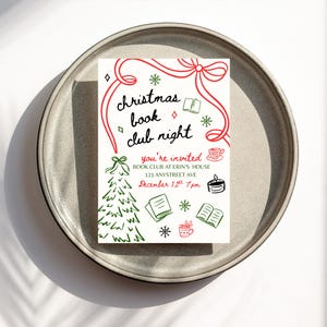 May include: A white invitation card on a gray plate, featuring the text "christmas book club night" in black script with red accents. The card includes illustrations of a Christmas tree, books, and snowflakes. The invitation is for a book club at Erin's house.