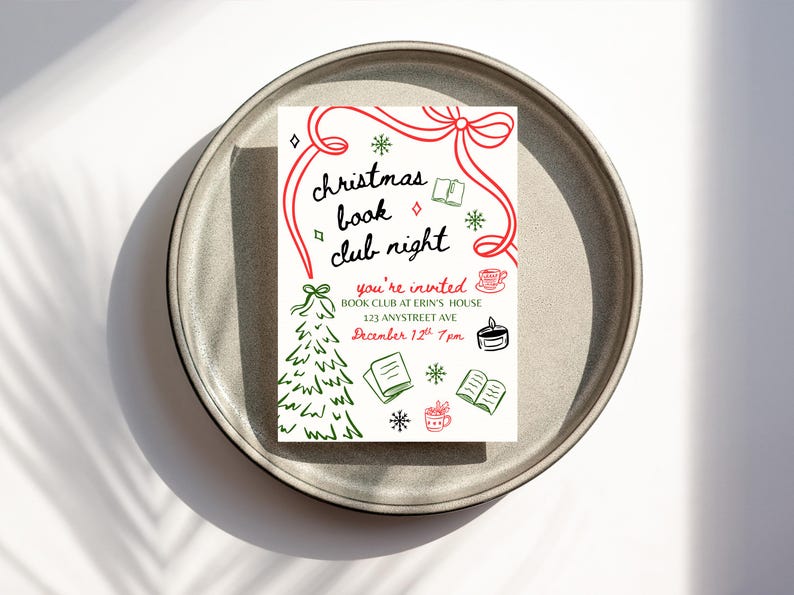 May include: A white invitation card on a gray plate, featuring the text "christmas book club night" in black script with red accents. The card includes illustrations of a Christmas tree, books, and snowflakes. The invitation is for a book club at Erin's house.