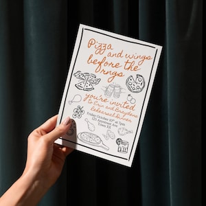 May include: A white invitation card with black and orange text and illustrations. The text reads "Pizza and wings before the Orngs" and invites guests to a rehearsal dinner. The card is held by a person.