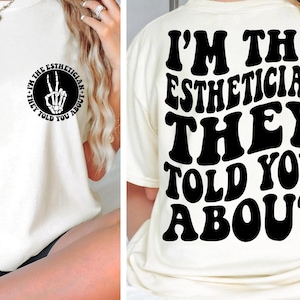 Puede incluir: Camiseta blanca con texto negro que dice "I'm the Esthetician They Told You About". El texto está en un estilo de fuente retro. La parte posterior de la camiseta tiene un signo de paz con una mano de esqueleto.