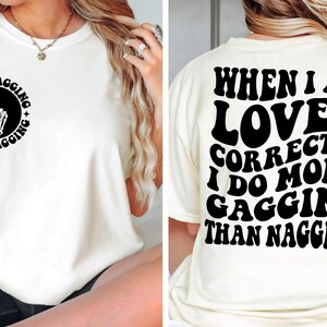 May include: White t-shirt with a black graphic on the front that says "Less Nagging More Gagging" with a peace sign made of bones. The back of the shirt says "When I am Loved Correctly I do More Gagging Than Nagging".