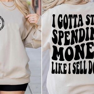 以下が含まれることがあります： 「I gotta stop spending money like I sell dope」と黒で書かれたグラフィックプリントが施されたベージュのスウェットシャツです。