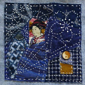 May include: A square textile collage featuring various shades of blue fabric patches joined with white sashiko-style stitching. The center displays a printed image of a person in traditional attire, while a wooden yin-yang button is attached.