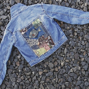 May include: A blue denim jacket with a patchwork design on the back. The patches are made of different fabrics and colors, including blue, green, red, and white.