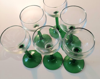 May include: Six clear glass wine glasses with rounded bowls and vibrant green stems and bases are arranged on a white surface. The glasses are empty and appear to be clean, with a classic design.