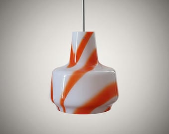 May include: A pendant light fixture featuring a bell-shaped glass shade with a smooth white base and bold, diagonal orange swirl patterns. The shade is suspended from a thin, straight metal rod extending from the top center of the glass.
