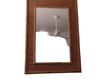 May include: Rectangular mirror with a woven bamboo frame. The frame is a warm brown color, and the mirror reflects a white ceiling and a ceiling fan. The mirror is a decorative item.