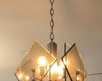 May include: A ceiling-mounted chandelier featuring a central metal frame with four square amber-tinted glass panels arranged in a geometric pattern. The fixture is suspended by a metal chain and includes multiple exposed light bulbs inside.
