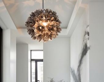 May include: A modern, spherical chandelier with a layered, petal-like design. The light fixture is suspended from the ceiling and casts a warm glow. The color palette is neutral, with shades of brown and beige.