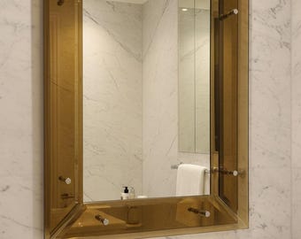 May include: A rectangular wall mirror featuring a wide, amber-tinted glass frame with beveled edges. The frame is secured to the wall with four prominent, cylindrical metal standoffs with flat, circular caps at each corner of the glass border.