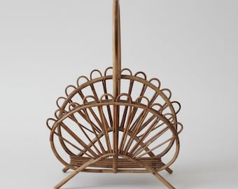 May include: A vintage rattan magazine rack with a handle. The rack features a fan-like design with curved supports and a sturdy base. The natural brown color of the rattan gives it a warm, inviting feel. This decorative piece is perfect for storing magazines and newspapers.