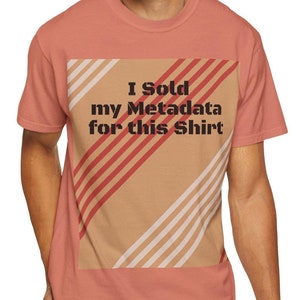 Puede incluir: Una camiseta de color coral con el texto "I Sold my Metadata for this Shirt" en negro. La camiseta presenta un cuadrado beige con rayas diagonales rojas y blancas. La persona lleva vaqueros azules.