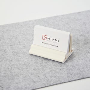 Puede incluir: Porta tarjetas de visita blanco con una tarjeta de visita blanca que dice "Dimiam Design Studio" y "Making your business grow".