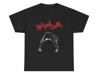 May include: Black t-shirt featuring the text "New York Dolls" in red script above a white line drawing of a person bending over. The graphic is centered on the front of the shirt.