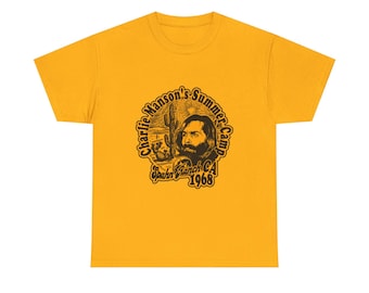 Könnte beinhalten: Senfgelbes T-Shirt mit einem kreisförmigen Grafikdesign mit einem Porträt eines Mannes mit Bart, einer Wüstenlandschaft und dem Text "Charlie Manson's Summer Camp Spahn Ranch CA 1968."