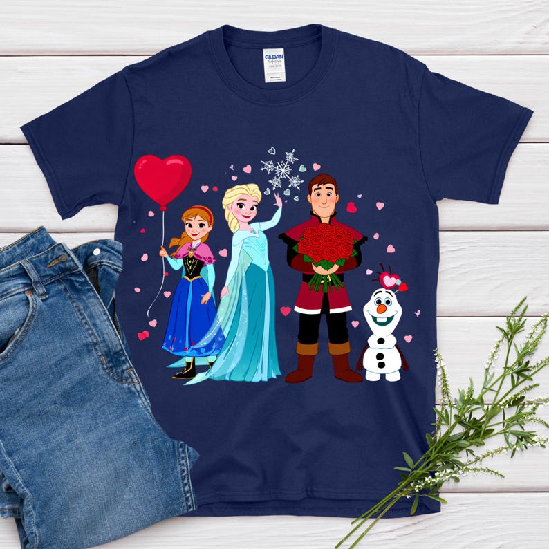 Pu&ograve; includere: T-shirt blu navy con una grafica a cartoni animati di personaggi di un popolare film d'animazione. Il design include un palloncino a forma di cuore rosso, un fiocco di neve e un bouquet di rose rosse. La maglietta &egrave; mostrata con un paio di jeans.