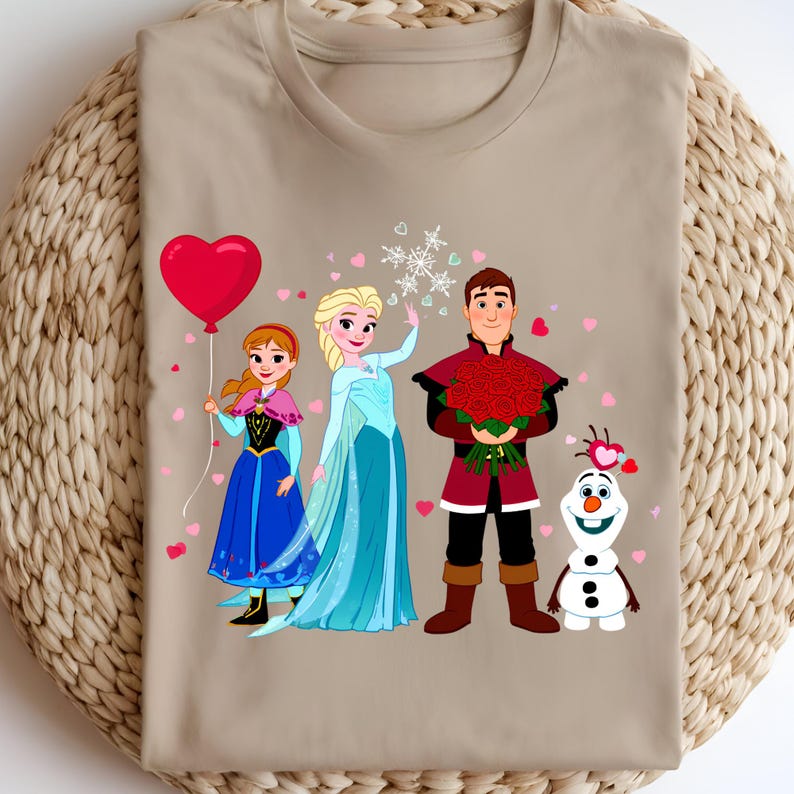 Pu&ograve; includere: Una maglietta beige con un'illustrazione di personaggi del film Frozen. Il design include Anna con un palloncino a forma di cuore rosso, Elsa, Kristoff con rose e Olaf. Cuori rosa e fiocchi di neve sono sparsi.