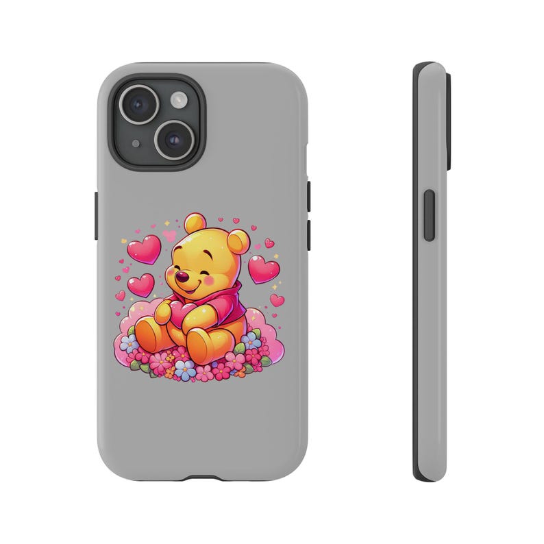 Puede incluir: Una funda de iPhone gris con una ilustraci&oacute;n de Winnie de Pooh. Winnie de Pooh est&aacute; sosteniendo un coraz&oacute;n y rodeado de corazones rosas y flores.