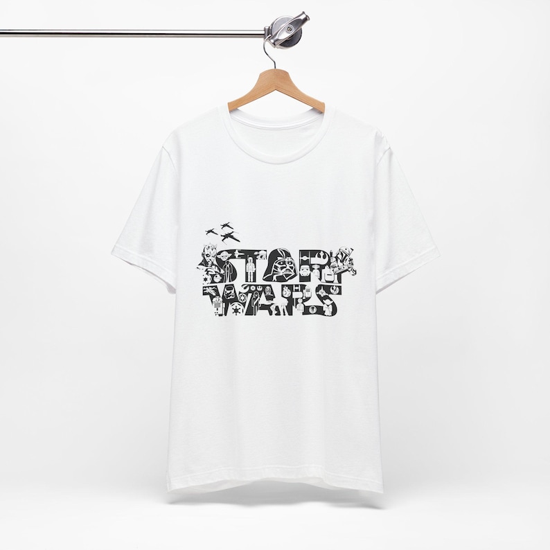 Może przedstawiać: Biała koszulka z czarno-białym nadrukiem graficznym sł&oacute;w "STAR WARS" utworzonym z r&oacute;żnych postaci i symboli Gwiezdnych Wojen.