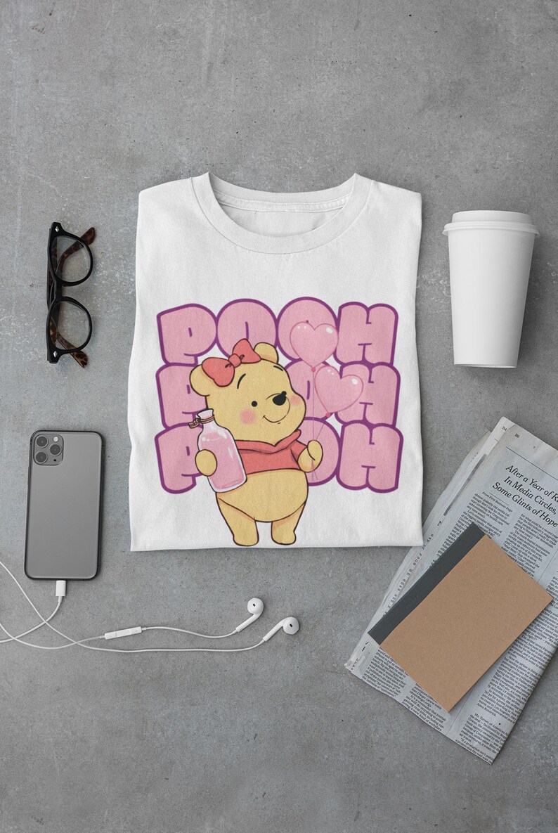 May include: White t-shirt with a cartoon image of Winnie the Pooh holding a bottle of honey and pink heart balloons. The text "POOH" is repeated in pink letters around the image.