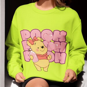 May include: A bright yellow sweatshirt with a pink graphic of Winnie the Pooh holding a bottle and balloons. The text "POOH POOH POOH" is printed in pink.