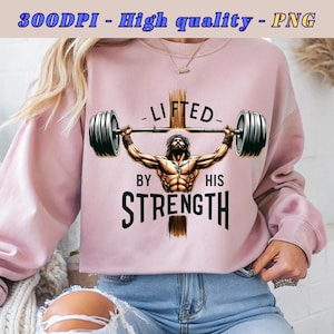 Pode incluir: Uma camisa de moletom rosa com um gráfico de um homem musculoso levantando uma barra com uma cruz atrás dele. O texto no gráfico diz "Lifted by His Strength".