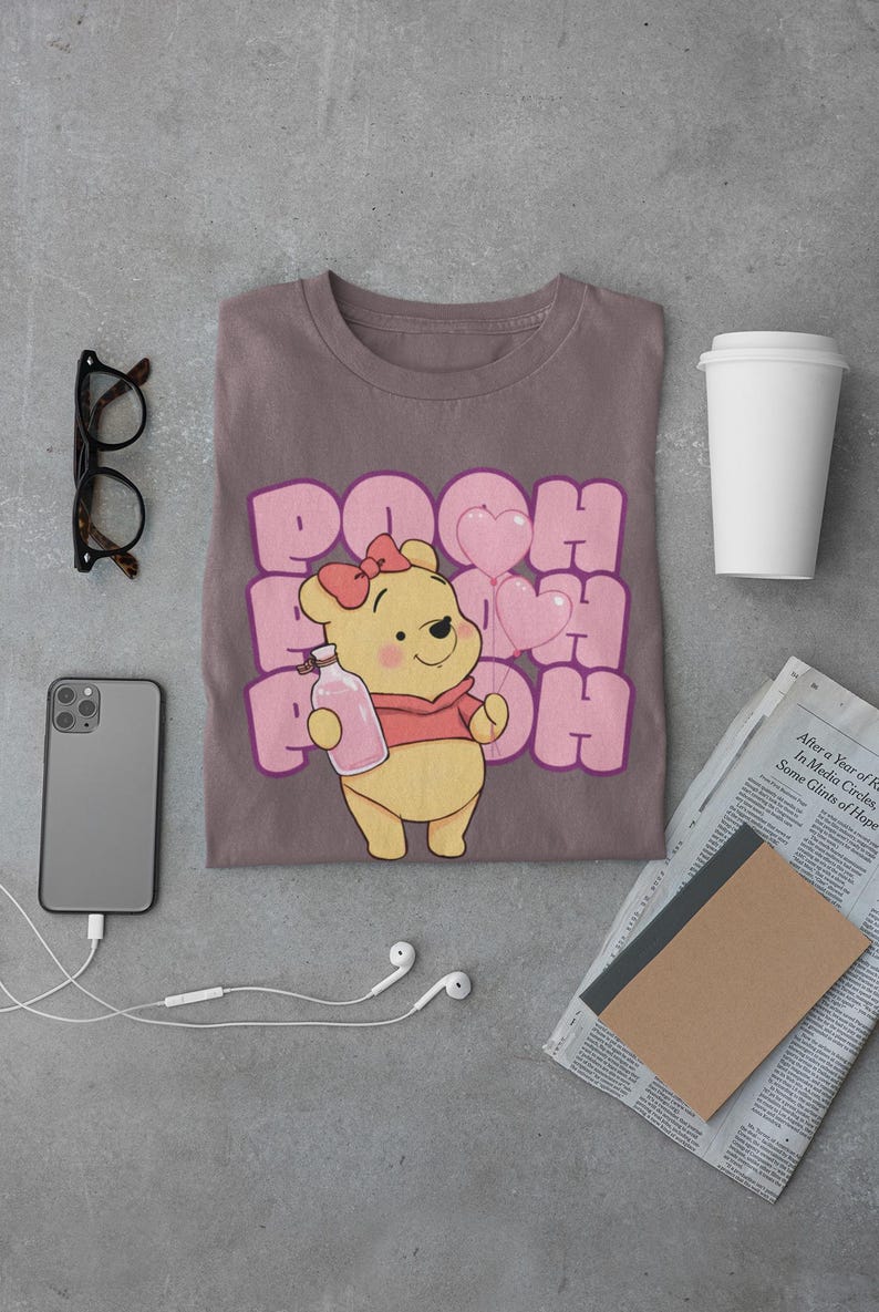 May include: A brown t-shirt with a pink graphic of Winnie the Pooh holding a bottle and pink balloons. The text "POOH" is repeated in pink letters.