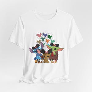 Puede incluir: Camiseta blanca con un estampado gr&aacute;fico de Stitch, Baby Yoda y Groot sosteniendo globos de Mickey Mouse. Los personajes llevan orejas de Mickey Mouse.