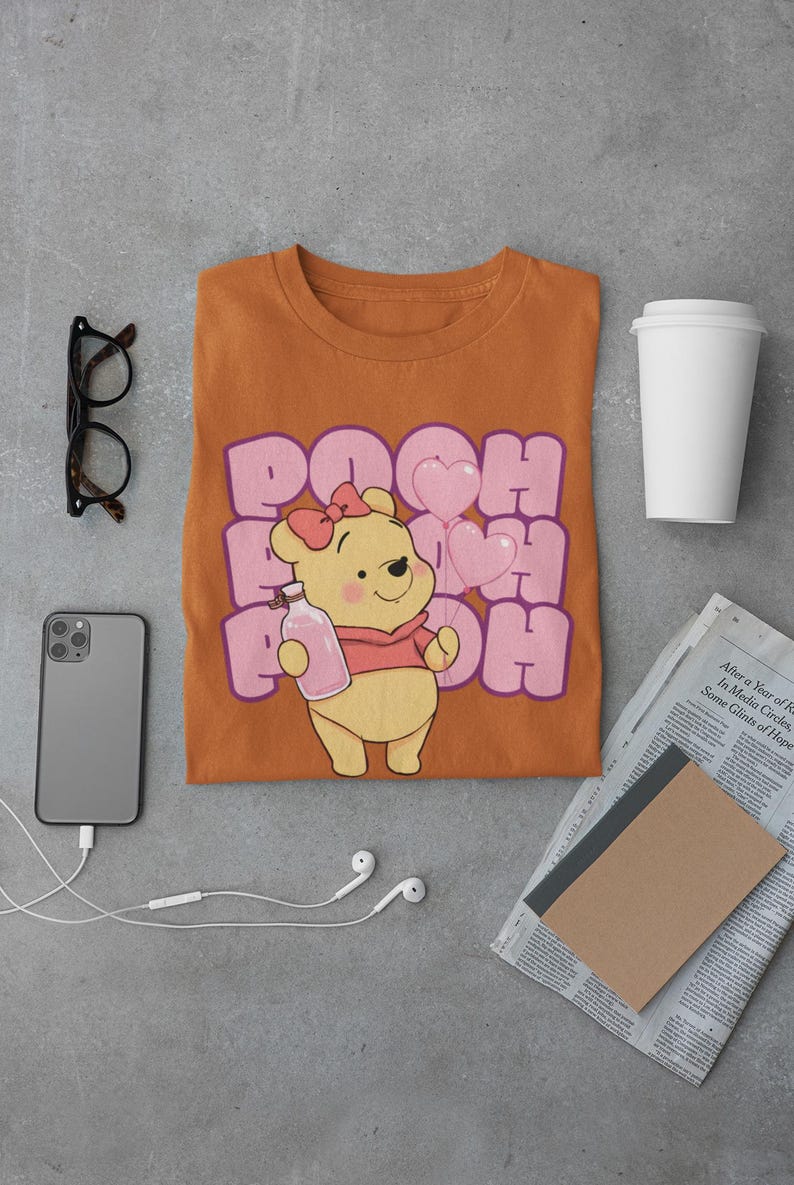 May include: A brown t-shirt with a cartoon image of Winnie the Pooh holding a bottle and pink heart balloons. The text "POOH" is printed in pink and purple letters.