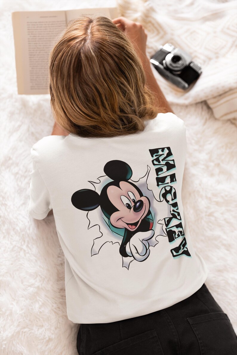 以下が含まれることがあります： 白いTシャツに、穴から顔を出したミッキーマウスのグラフィックと、横に「MICKEY」と縦書きで書かれた文字がプリントされています。