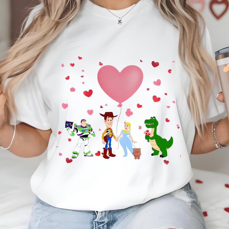 May include: White t-shirt featuring cartoon characters Buzz Lightyear, Woody, Cinderella, and Rex, with a pink heart balloon and scattered hearts. The design is a Valentine's Day theme.
