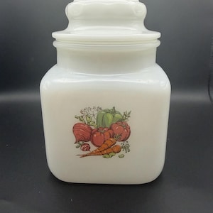Peut inclure: Pot à provisions en verre blanc avec couvercle, orné d'une illustration de légumes, dont des tomates, des carottes et un poivron vert. Le pot est de forme carrée.