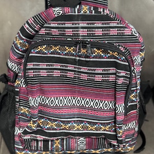 May include: A colorful backpack with a geometric pattern in shades of black, red, white, and yellow. The backpack has a front zippered pocket, side mesh pocket, and black shoulder straps.