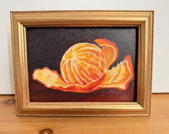 Puede incluir: Una pintura al óleo de una mandarina parcialmente pelada sobre un fondo oscuro. La fruta muestra segmentos de color naranja y amarillo vibrantes con una cáscara texturizada. La obra está enmarcada en un marco rectangular dorado y ornamentado.